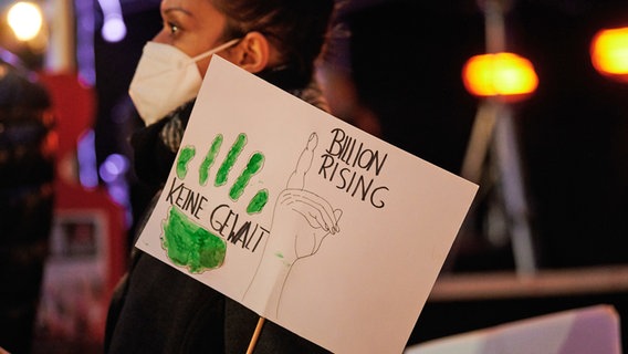 Eine Frau, die eine FFP2-Maske trägt, hält ein Plakat, auf dem "Billion Rising" und "Keine Gewalt" steht. © picture alliance/dpa | Annette Riedl 