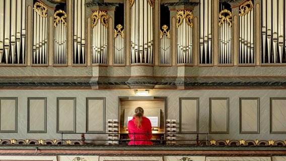 Eine Frau in roter Jacke sitzt an einer Orgel. © imageBROKER/Raimund Kutter via w 