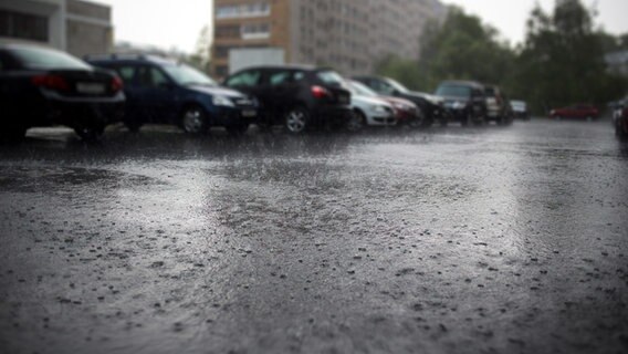 Autos stehen im Regen auf einem Parkplatz, im Hintergrund ein Hochhaus. © Fotolia 
