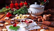 Eine Schale mit Barszcz (Rote-Beete-Suppe) und davor eine mit Piroggi auf einem festlich gedeckten mit Adventskranz geschmückten polnischen Weihnachtstisch © imago / xDar1930x Panthermedia27375365 