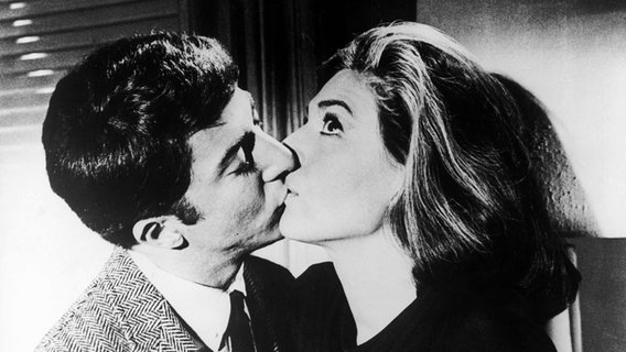 Ein junger Mann mit Krawatte küsst eine ältere Frau, die ihre Augen weit aufgerissen hat (Filmszene aus "Die Reifeprüfung" mit Dustin Hoffman und Anne Bancroft) © imago/United Archives 