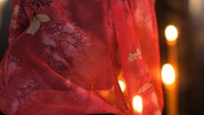 Ansicht einer Frau von hinten aufgenommen mit einem roten Kopftuch vor dunklem Hintergrund mit zwei Kerzenlichtern. © picture alliance / dpa 