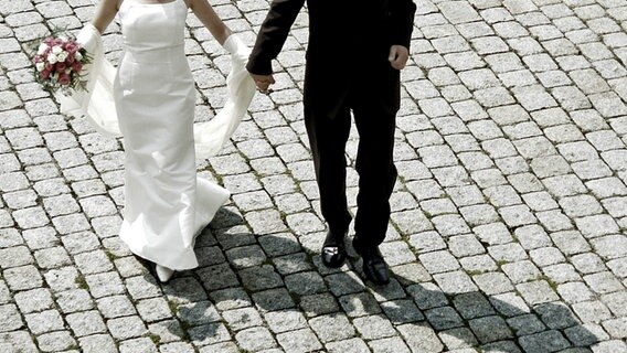 Ein Brautpaar geht Hand in Hand über Kopfsteinpflaster © photocase Foto: Pip