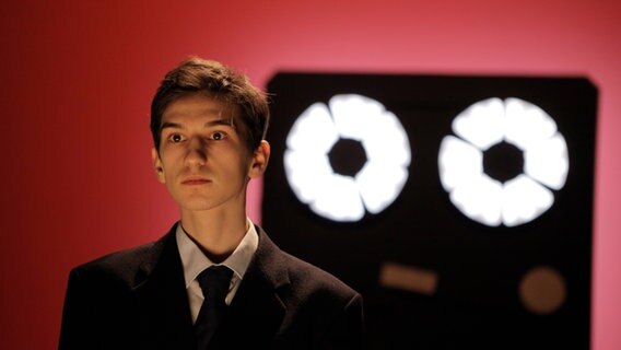 Ein junger Mann steht vor einem roten Hintergrund und wird von hinten angestrahlt. © © Silviu Ghetie Foto: Silviu Ghetie