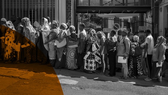 Etwa zwanzig Schwarze Menschen stehen dicht gedrängt in einer Reihe. Sie tragen unterschiedliche Kopfbedeckungen und in den Händen Papiere. © ARD Foto: Morgan Fache