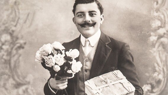Porträt eines jungen Mannes mit Blumen und einem Geschenk, ca. 1920. © colourbox 