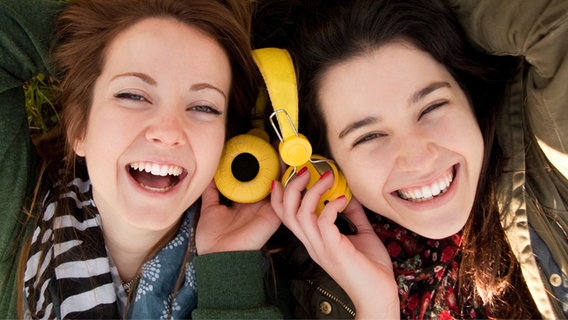 Zwei junge Frauen liegen auf dem Rasen und hören gemeinsam mit einem Kopfhörer. © ASIFE / photocase.de Foto: ASIFE
