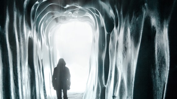 Ein junger Mann mit Kapuze von hinten. Er läuft durch einen Tunnel dem Licht entgegen. Um ihn herum ist enges Gewölbe, das feucht glänzt. © joexx / photocase.de 