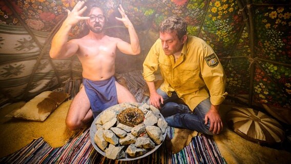 Flötzinger (Daniel Christensen) und Franz (Sebastian Bezzel) vor einem Feuer auf einem Steinhaufen. © Constantin Film 