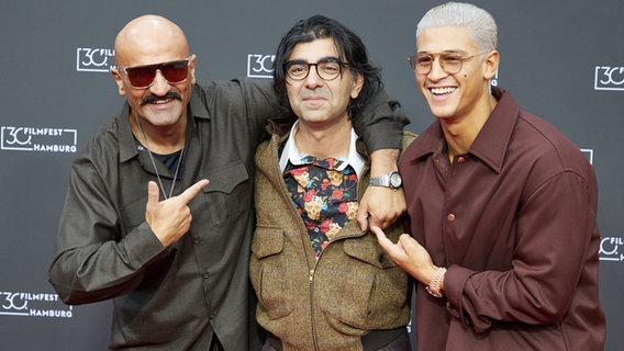 Der Rapper Xatar, Fatih Akin, Regisseur, und Emilio Sakraya, Schauspieler, stehen auf dem Roten Teppich zu ihrem Film "Rheingold" im Cinemaxx. © picture alliance/dpa | Georg Wendt 