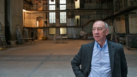Ein Mann mit blauem Hemd und dunklem Jackett schaut seitlich, er steht in einer großen alten Halle, dahinter sind hellere Fenster und Stockwerke zu erkennen - Rainer Rother in den Räumen der Deutschen Kinemathek in Berlin © Erik Weiss / Deutsche Kinemathek Foto: Erik Weiss
