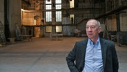 Ein Mann mit blauem Hemd und dunklem Jackett schaut seitlich, er steht in einer großen alten Halle, dahinter sind hellere Fenster und Stockwerke zu erkennen - Rainer Rother in den Räumen der Deutschen Kinemathek in Berlin © Erik Weiss / Deutsche Kinemathek Foto: Erik Weiss