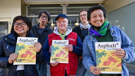 Daniella Fitriab (l-r), Iswanto Hartono (beide vom Künstlerkollektiv Ruangrupa), Stefan Marx (Verkäufer der Straßenzeitung "Asphalt"), Volker Macke (Redaktionschef "Asphalt") und Reza Afisina (Ruangrupa) präsentieren vor dem ruruHaus die Oktober-Ausgabe der "Asphalt" mit der kompletten Künstlerliste der ausstellenden Künstlerinnen und Künstler der "documenta fifteen". © picture alliance/dpa Foto: Uwe Zucchi