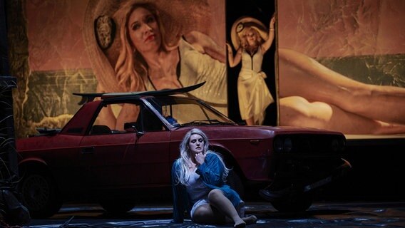 Eine blonde Frau sitzt vor einem roten Auto auf dem Boden © Staatstheater Braunschweig/ Thomas M. Jauk Foto: Thomas M. Jauk