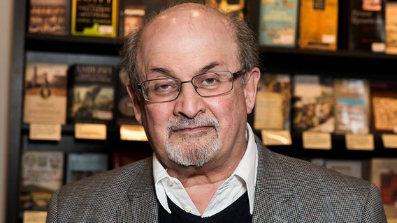 Der Autor Salman Rushdie vor einer Bücherwand © Grant Pollard/Invision/AP/dpa 