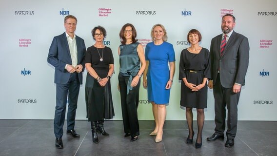 Zwei Männer und vier Frauen stehen vor einer Fotowand und lächeln in die Kamera © NDR Foto: Axel Herzig