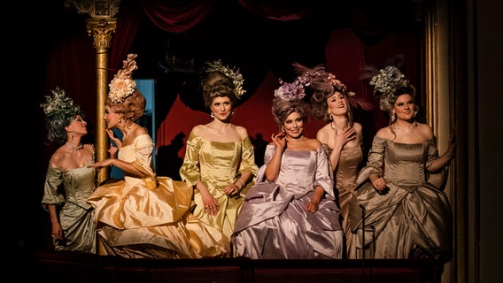 In einer Theaterloge stehen sechs gut gelaunte Frauen, die barocke Kostüme tragen. © Alciro Theodoro da Silva 