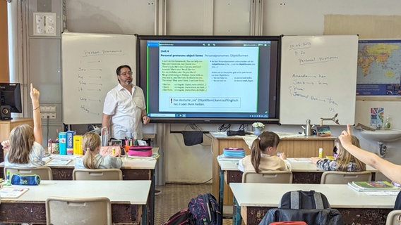 Ein Grundschullehrer steht vor einer Klasse, neben ihm ein Whiteboard mit Informationen an der Tafel © Radio Bremen/Claudia Euen 