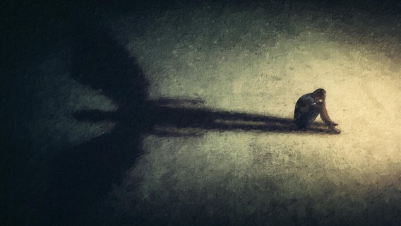 Surreales Gemälde eines Mannes, der allein und isoliert in einem dunklen Raum sitzt und den Schatten eines mächtigen Schutzengels wirft. Eine Metapher für innere Stärke. Introvertierte Person hat einen imaginären Freund gefunden © picture alliance / imageBROKER | PsychoShadow 