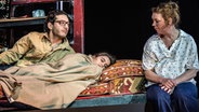 Mehmet Ateşçi und Lina Beckmann betrachten ein Kind das krank im Bett liegt. © Deutsches Schauspielhaus/Knut Koops 