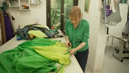 Eine Frau zerschneidet ein grünes Zelt. © NDR 