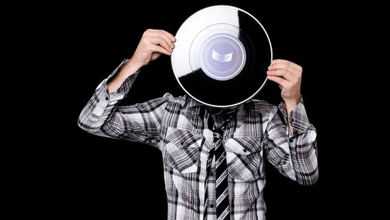 Vor schwarzem Hintergrund hält sich ein Mann eine Schallplatte vor sein Gesicht. © Z2sam 