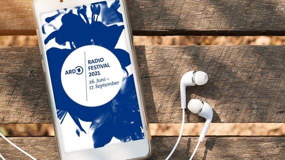 Ein Mobiltelefon mit Kopfhörern liegt auf einer Bank, auf dem Display wird das Logo des ARD Radiofestivals 2021 angezeigt. © ARD 