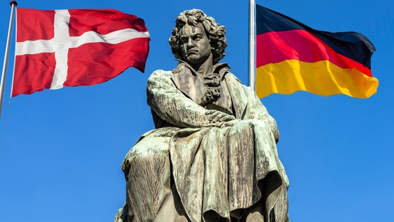 Das Denkmal Ludwig van Beethovens vor strahlend blauem Himmel, im Hintergrund die Dänische und Deutsche Flagge (Montage) © picture alliance, Colourbox Foto: Peter Schickert, Eugen Wais