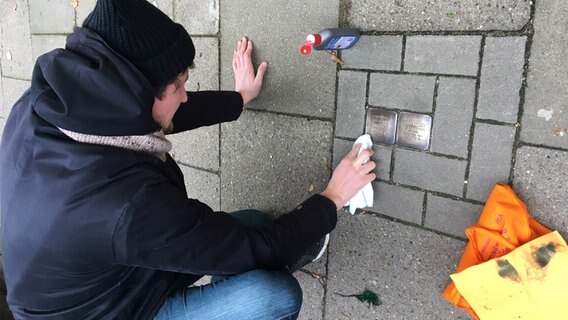 Ein junger Mann putzt und poliert zwei Stolpersteine in Hamburg. © Laura Sonnefeld Foto: Laura Sonnefeld