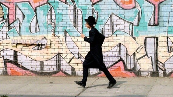 Ein junger orthodoxer Jude läuft an einer mit einem Grafitti bemalten Häuserwand in Williamsburg/ Brooklyn entlang. © imago/ Lem 