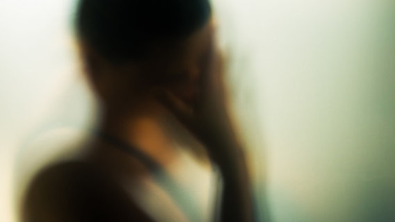 Verschwommene Silhouette einer Person mit Hand vor dem Gesicht. © photocase / Jeeni Foto: Jeeni