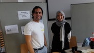 Ein junger Mann und eine junge Frau hinter einem Stand  in der Uni lächeln in die Kamera. © NDR Foto: Hans Stallmach