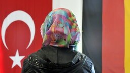 Ein Frau mit Kopftuch sitzt am in einer Moschee vor einer türkischen und einer deutschen Fahne. © dpa Foto: Boris Roessler