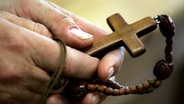 Hand hält einen hölzernen Rosenkranz mit Kreuz daran. © picture-alliance/ dpa/dpaweb 