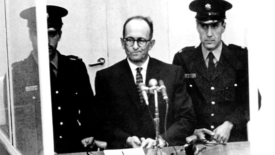 NS-Kriegsverbrecher Adolf Eichmann (2.v.l.) steht während seiner Vernehmung am ersten Prozesstag vor dem Bezirksgericht in Jerusalem (Archivfoto vom 11.04.1961). © picture-alliance / dpa 