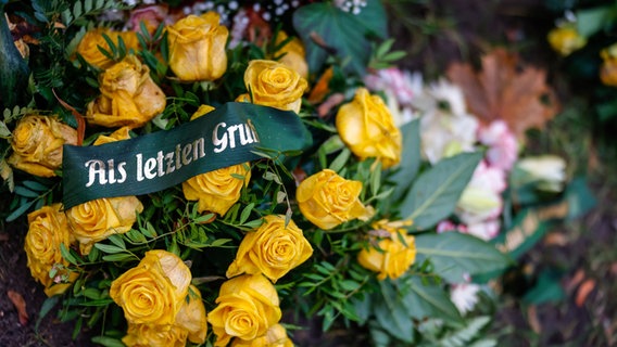 Ein Strauß gelbe Rosen auf einem Grab, daran ein Spruchband: "Zum letzten Gruß". © photocase / Alpenfux Foto: Alpenfux