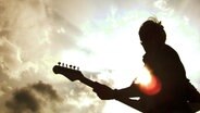Die Silhouette einer Person mit Gitarre steht vor strahlend hellem Himmel. © photocase / sto.E Foto: sto.E