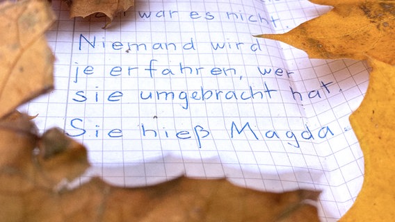 Ein Zettel liegt im Herbstlaub. Darauf steht: "Niemand wird je erfahren, wer sie umgebracht hat. Sie hieß Magda."  Foto: Konrad Winkler