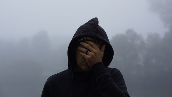 Ein Mann mit Kapuzenpulli hält sich die Hand vor's Gesicht. © photocase | Bernd Vonau Foto: Bernd Vonau