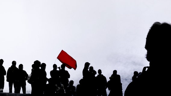 Die Silhouette einer Gruppe Menschen mit einer roten Flagge, am Himmel ein Hubschrauber. © photocase / Martin Koos Foto: Martin Koos