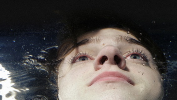 Das Gesicht eines jungen Mannes liegt mit offenen Augen knapp über der Wasseroberfläche. © Photocase Foto: Meikel.inSpirit
