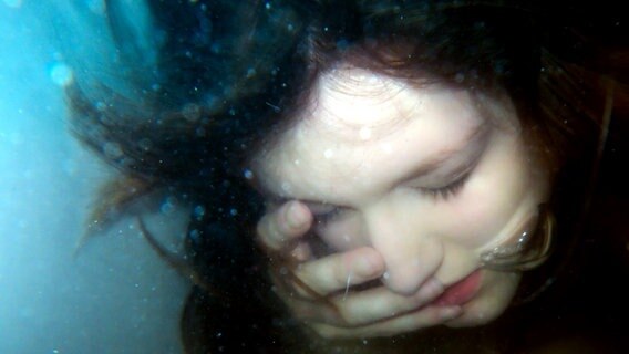 Eine junge Frau unter Wasser hält sich die Hand ins Gesicht. © Photocase Foto: froodmat