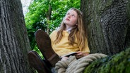 Ein Mädchens sitzt auf einem Baum. © LOOKSfilm 