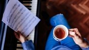 Person sitzt mit einer Tasse Kaffe in der Hand am Klavier © Photocase Foto: Eva Blanco Fotografia