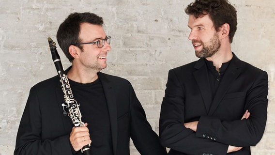 Zwei Männer lächeln sich an, der linke hält dabei noch eine Klarinette in der Hand, der rechte verschränkt die Arme. © Kaupo Nikkas Foto: Kaupo Nikkas
