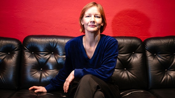 Sandra Hüller sitzt auf einem schwarzen Sofa ©  Oliver Dietze/dpa +++ dpa-Bildfunk Foto:  Oliver Dietze