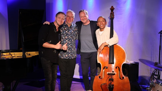 Vier Männer lächeln freundlich, sie stehen zwischen mehreren Musikinstrumenten. © Franziska Dieckmann / NDR Foto: Franziska Dieckmann / NDR