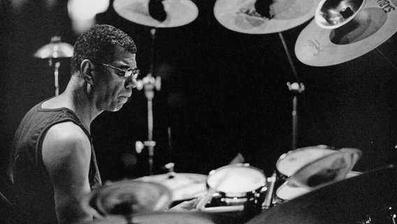 Ältere schwarz-weiß Aufnahme von Jack DeJohnette, der im Profile zu sehen ist und Schlagzeug spielt. © Robert Masotti Foto: Robert Masotti