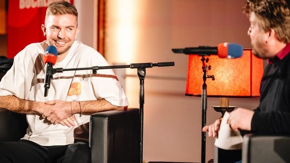 Fußballweltmeister Christoph Kramer und Moderator Alexander Solloch sitzen auf einer Bühne und schauen sich lachend an. © Literarischer Salon Hannover / Nerea Lakuntza Foto: Nerea Lakuntza