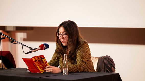 Deborah Feldman sitzt lesend vor einem Mikrofon an einem Tisch. © Nerea Lakuntza Foto: Nerea Lakuntza